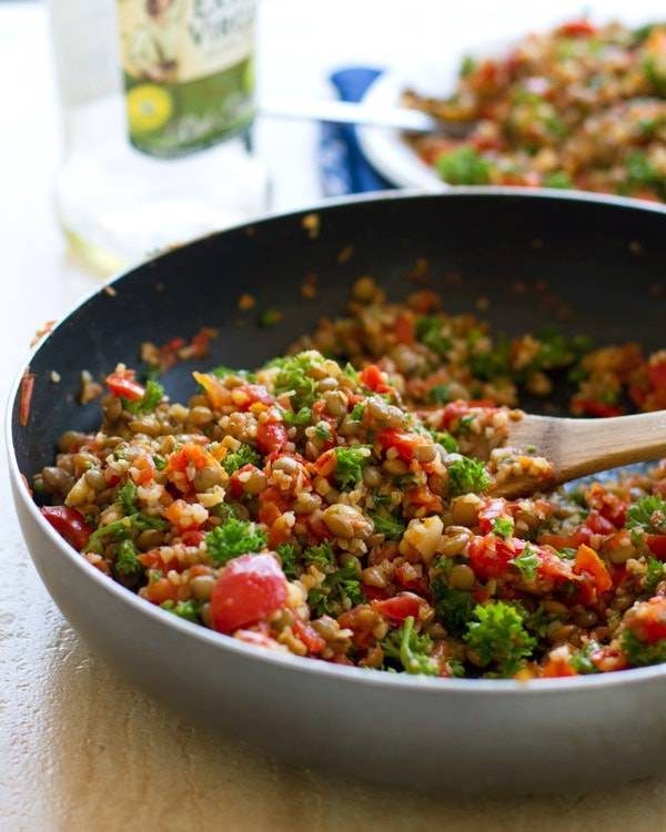 Garlic and tomato lentil salad in a skillet with a wooden spoon.