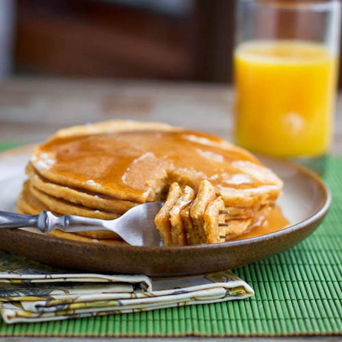 Stack of pancakes on a plate with a fork and a glass of orange juice.